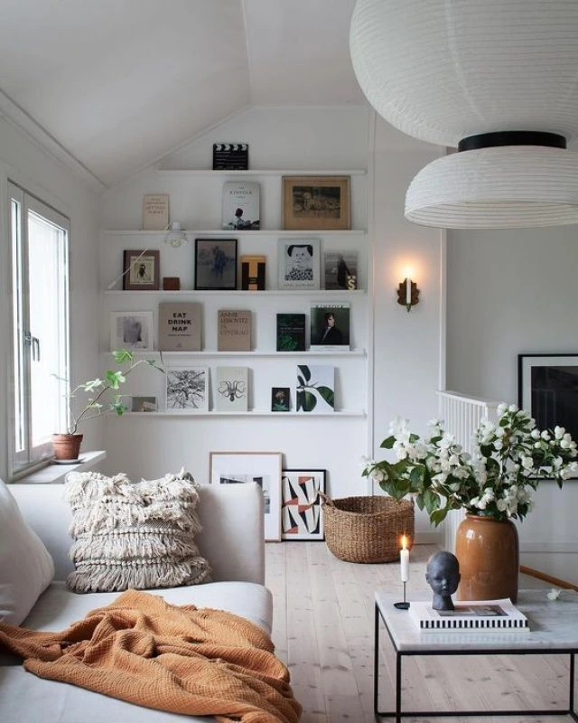 Sala de estar Boho Escandinavo com sofá claro, manta terrosa, almofada texturizada e prateleiras de livros, decoração natural e minimalista.