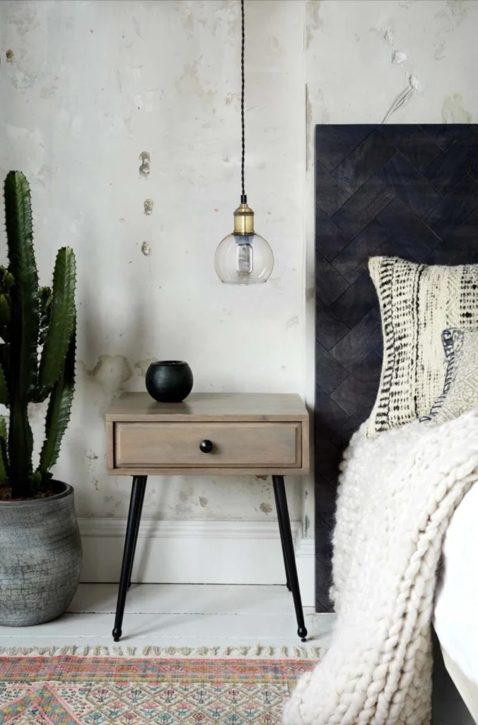 Quarto Boho Escandinavo com parede desgastada, criado-mudo de madeira, cacto em vaso e cama com manta de tricô.