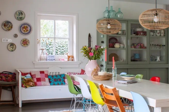 Sala de jantar Boho Escandinavo com cadeiras coloridas, luminárias de fibra e armário vintage.