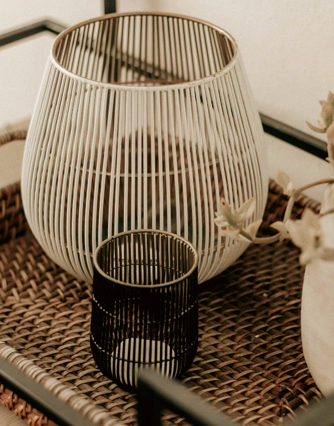 Lanternas decorativas em estrutura clara sobre bandeja de fibras naturais, composição de decoração nórdica escandinava com tons neutros e estilo minimalista.
