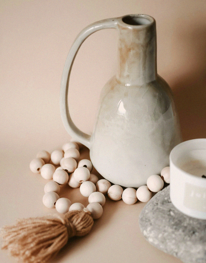 Vaso cerâmico minimalista com contas de madeira e vela decorativa em tons neutros, composição típica da decoração nórdica escandinava com estilo clean e natural.