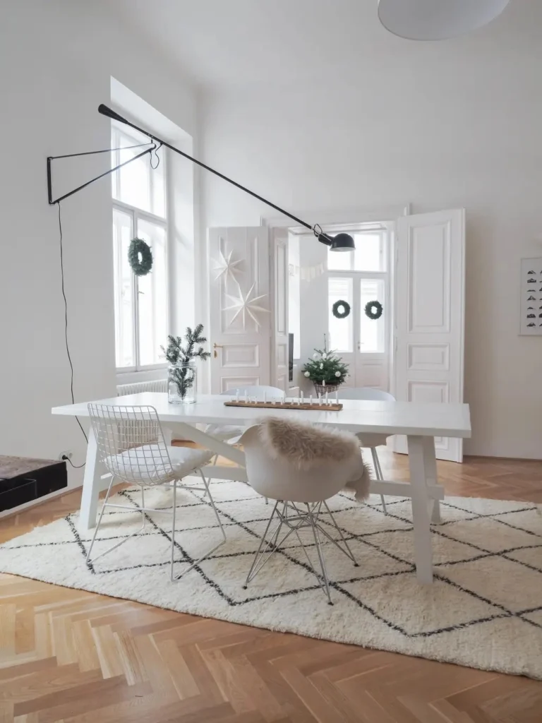 Sala de jantar escandinava com mesa branca, cadeiras modernas, tapete felpudo geométrico e decoração minimalista com luz natural.