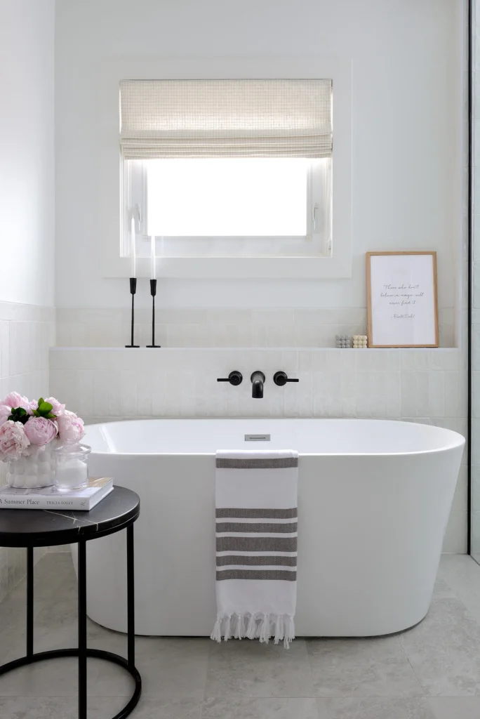 Banheiro Boho Escandinavo com banheira de imersão, paredes brancas e decoração minimalista com flores e velas.