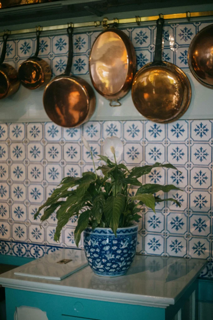 Lírio-da-paz em vaso azul estampado sobre bancada de cozinha com azulejos portugueses e panelas de cobre penduradas