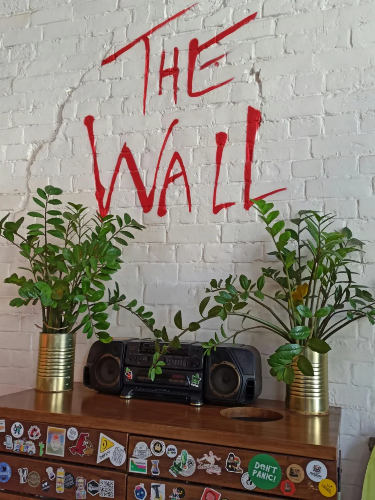 Zamioculcas em vasos metálicos dourados sobre aparador de madeira, em ambiente descolado com parede de tijolos brancos e grafite vermelho ‘The Wall