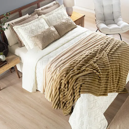 Cama com cobertor felpudo bege claro dobrado sobre a colcha branca e almofadas decorativas