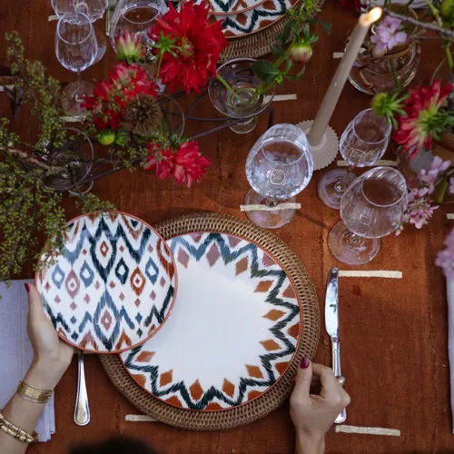 Mesa posta com pratos artesanais estampados em padrões geométricos coloridos, sobre sousplats de palha, criando uma atmosfera acolhedora na cozinha Boho.