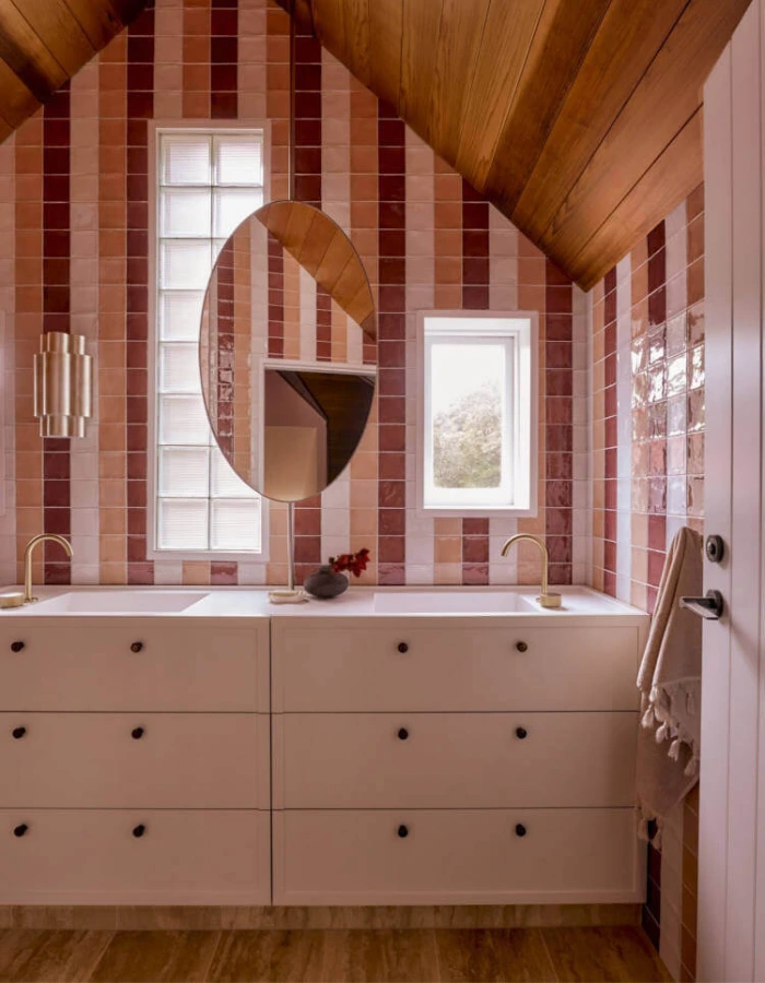 Banheiro pequeno e luxuoso com azulejos verticais em tons de rosa e teto de madeira, combinando cor, aconchego e sofisticação.