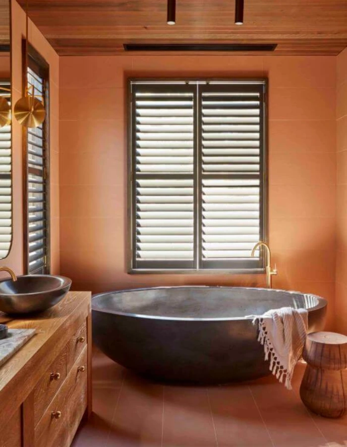 Banheiro pequeno e luxuoso com paredes terracota, banheira de pedra e teto de madeira, unindo conforto, elegância e design natural.