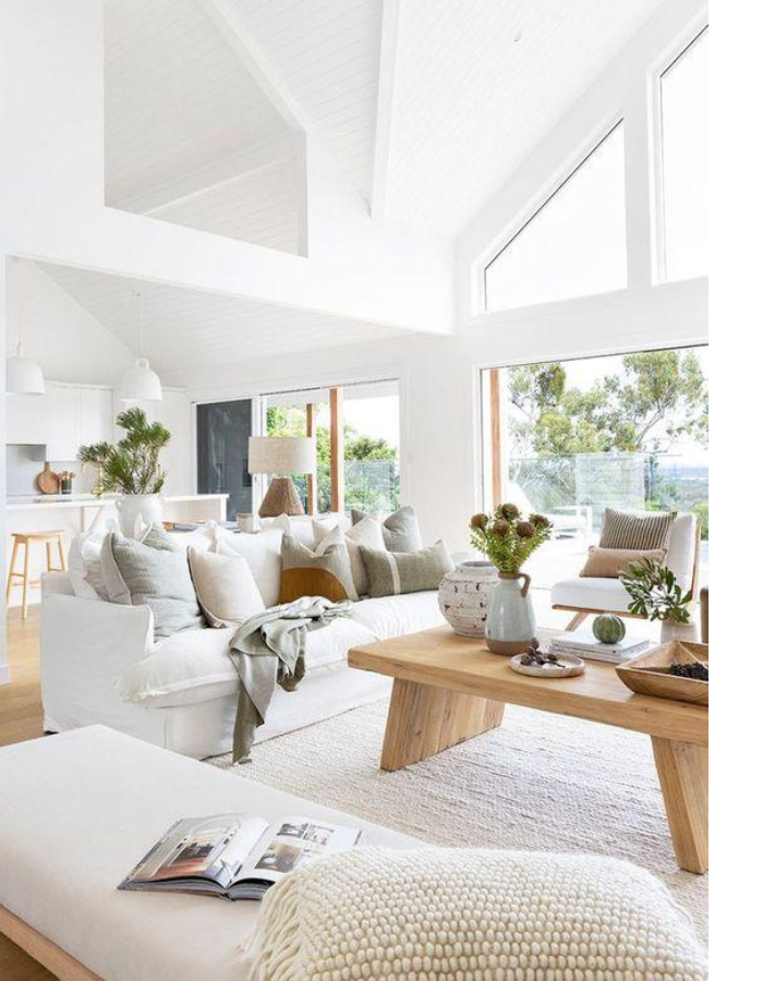 Sala de estar de casa clara e aconchegante com decoração clean, sofá branco, mesa de centro em madeira, tons naturais e ampla iluminação natural.