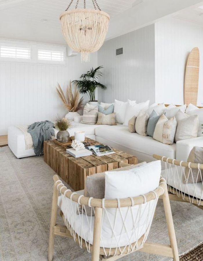 Sala de estar clara e aconchegante com sofá branco, almofadas neutras, mesa de centro em madeira, poltrona com fibras naturais e decoração clean com iluminação suave.
