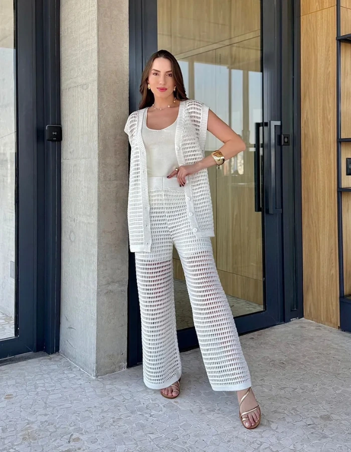 Mulher usando conjunto branco em tricot vazado com calça, colete e top, estilo praia minimalista elegante.